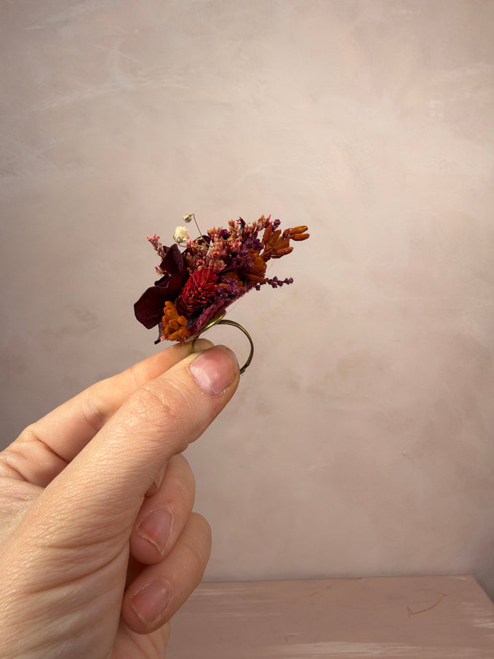 A hand holding a small dried flower ring against a soft beige textured background.
