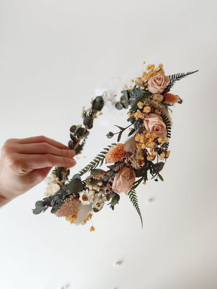 Floral wreath with eucalyptus and blush preserved roses held by a hand against a light background
