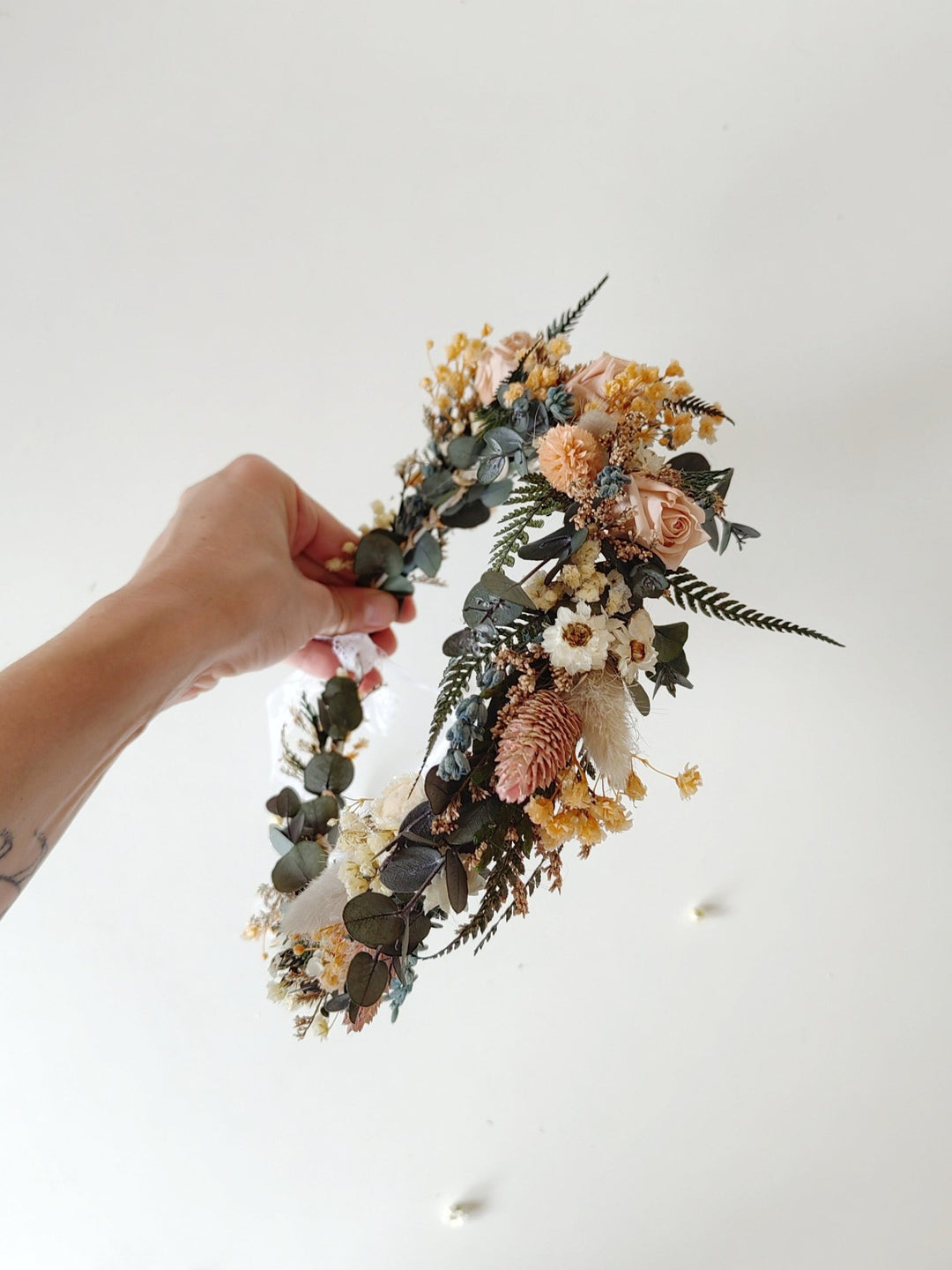 Hand holding a floral wreath in natural boho style in blush and green tones against a white background