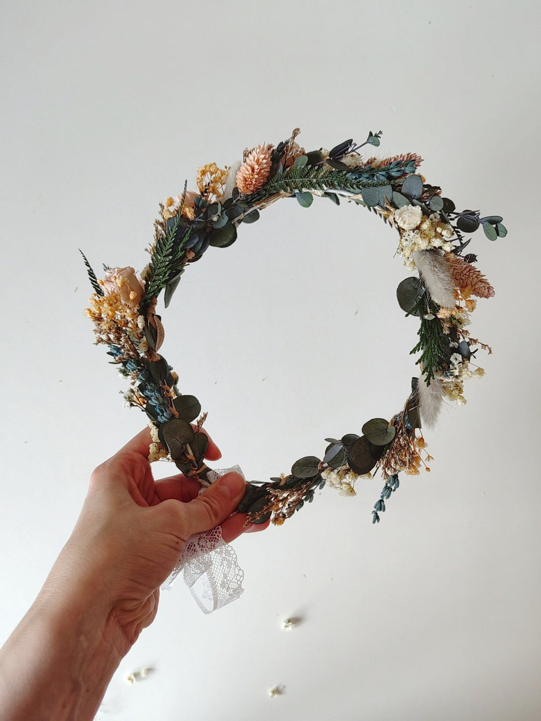 Hand holding a decorative floral crown against a plain background