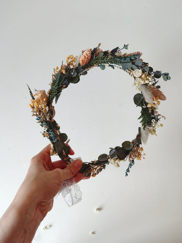 Hand holding a decorative floral crown against a plain background