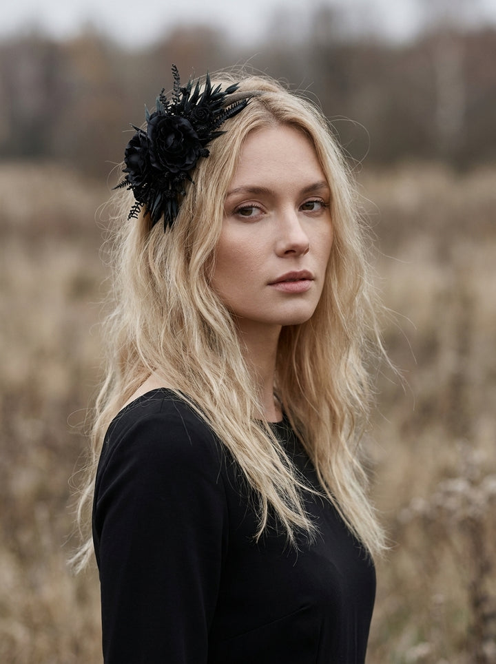 A blonde woman wearing a black floral headpiece and a black long-sleeve top, standing in a dry grassy field.