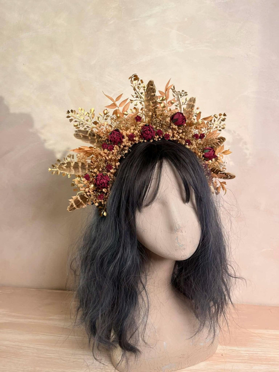 Mannequin head with a decorative cream and burgundy floral crown on a neutral background