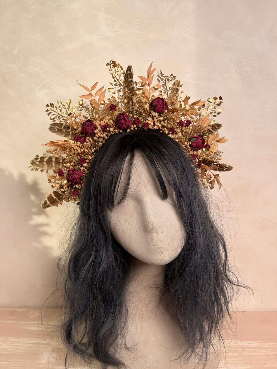 Mannequin head with dark hair wearing a decorative floral headpiece on a beige background