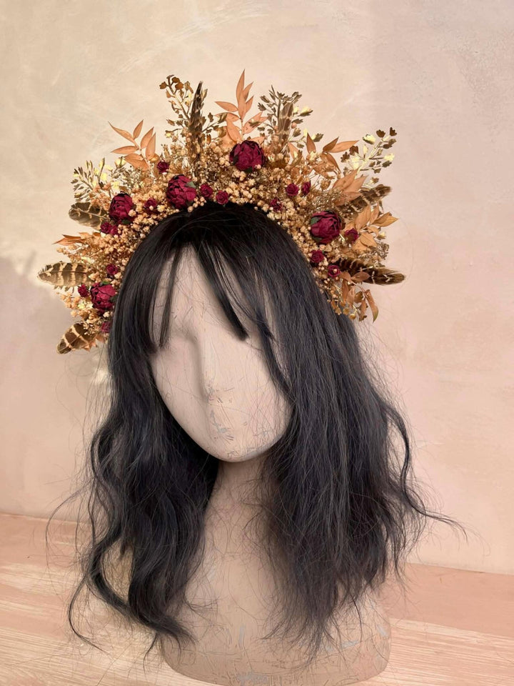 Floral headpiece with gold leaves and burgundy flowers on a mannequin head against a beige background