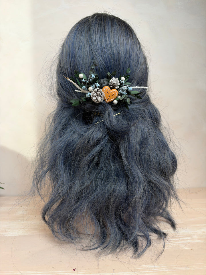 A long, wavy dark blue-gray wig displayed on a mannequin head, styled with a decorative hair accessory featuring greenery, small bluebberries, and a small heart.