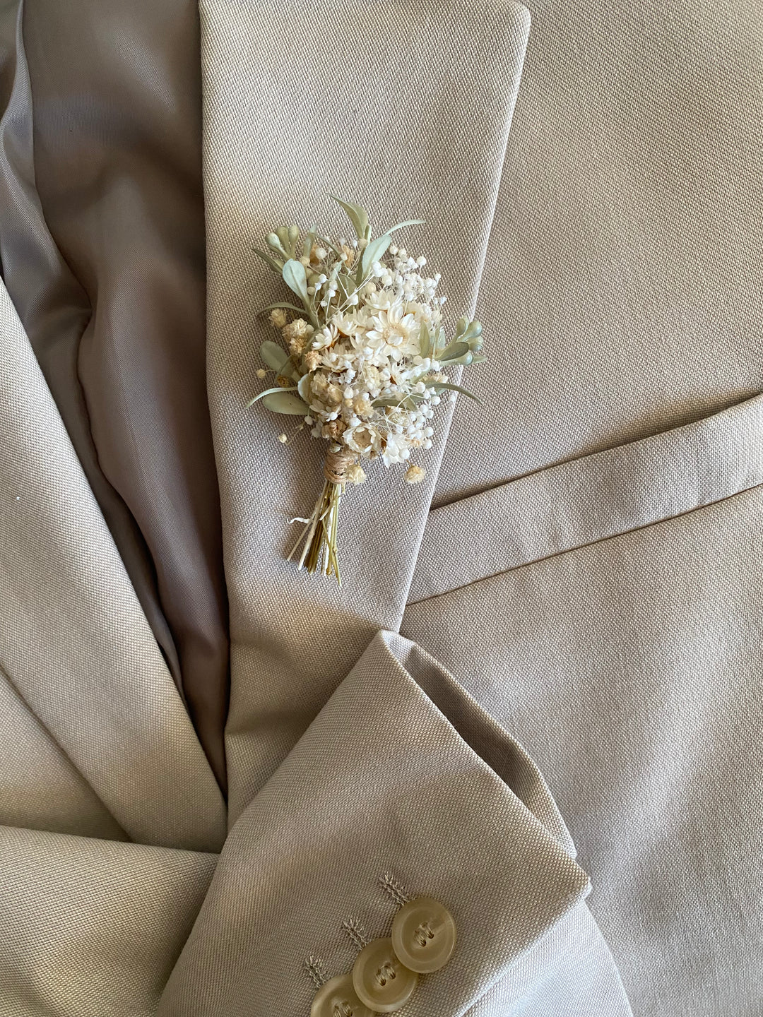 Floral boutonniere on a beige suit jacket with buttons.