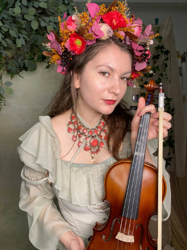 Woman holding a violin with floral headpiece and jewelry
