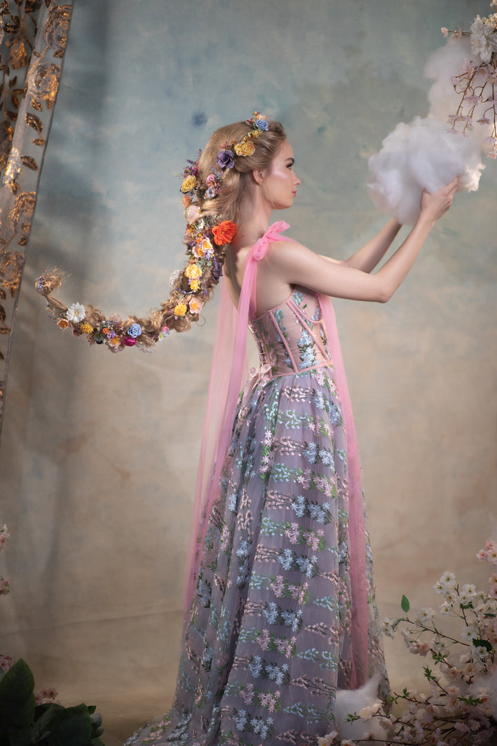 Woman in a floral dress with flower in hair  a textured wall with decorative elements.