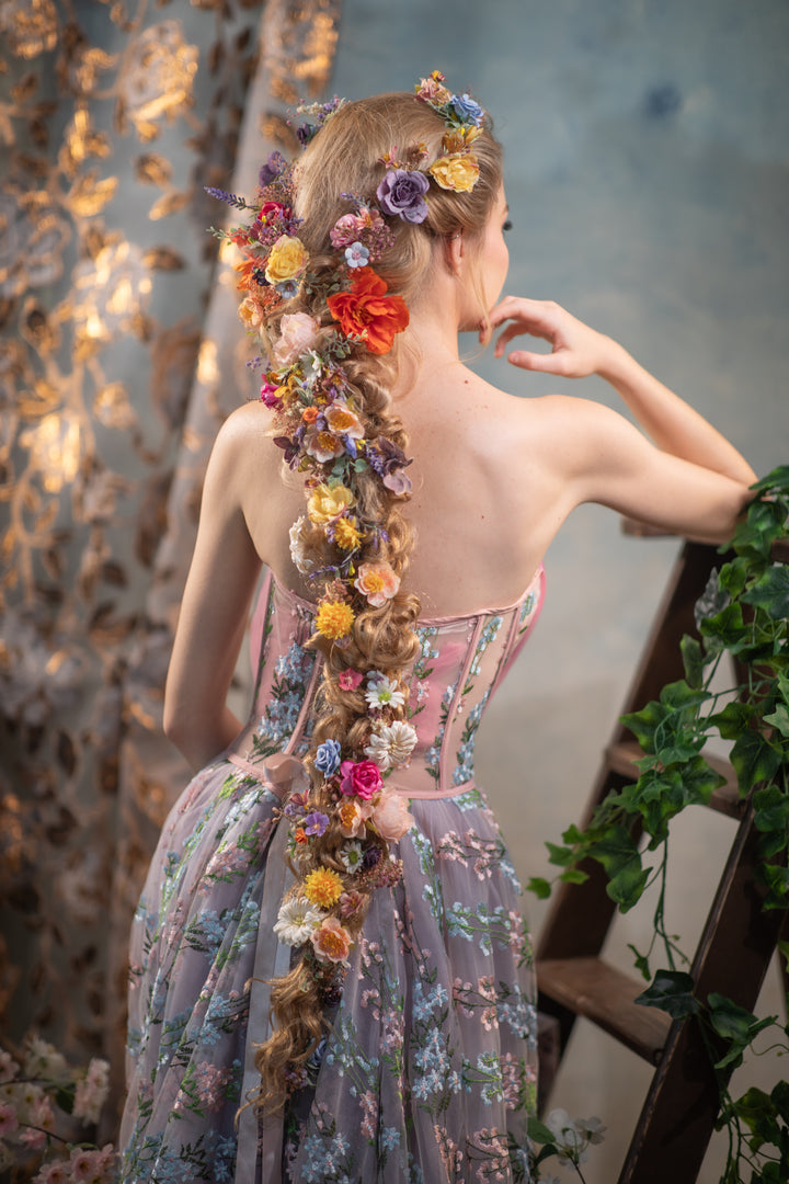 Woman with a floral hairpiece and dress standing against a textured wall.