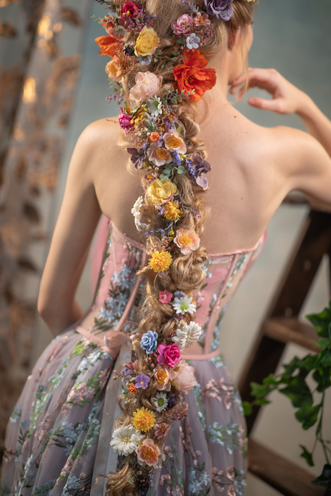 Woman with a floral hairpiece and dress in Rapunzel style, standing outdoors.