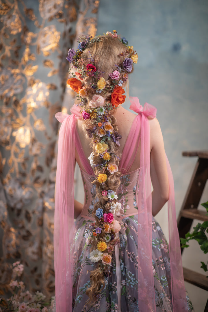 Woman with floral hair and dress standing against a textured wall.