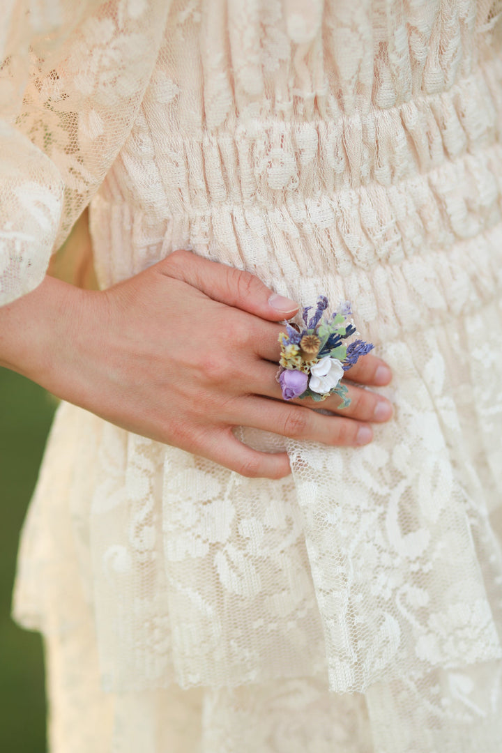 Hand holding a small flower ring in purple tones against a blurred background