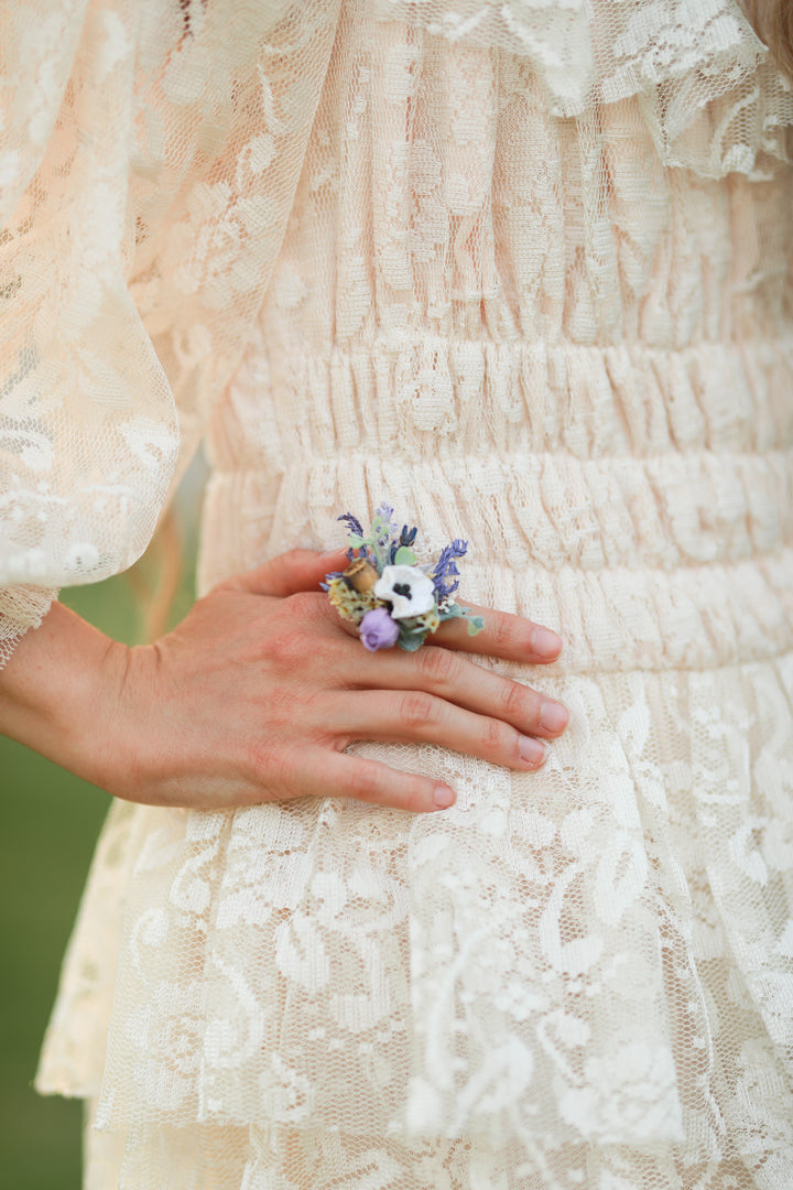 Close-up of a hand wearing a floral ring with a lace dress in the background