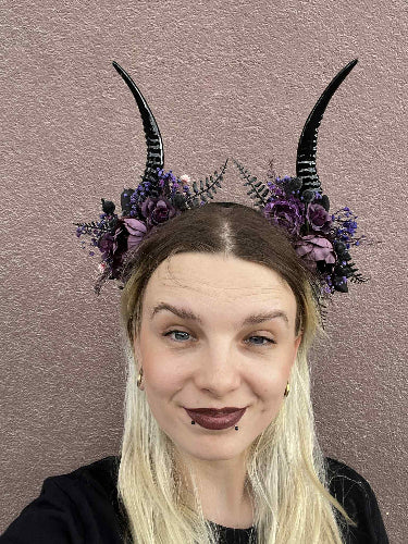 Person wearing black horns with purple flowers against a pink background