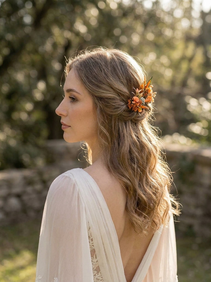 A woman in profile wearing a soft cream lace dress and a small orange floral hair accessory, photographed outdoors with a blurred natural background.
