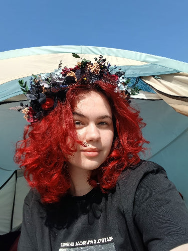 Person with red hair and floral headpiece in front of a tent