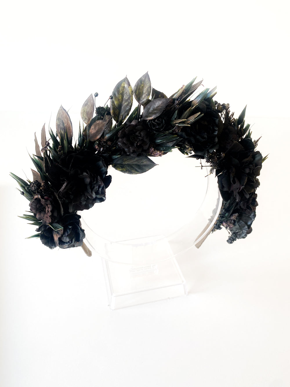 A black floral and leaf crown displayed on a clear acrylic stand against a plain white background.
