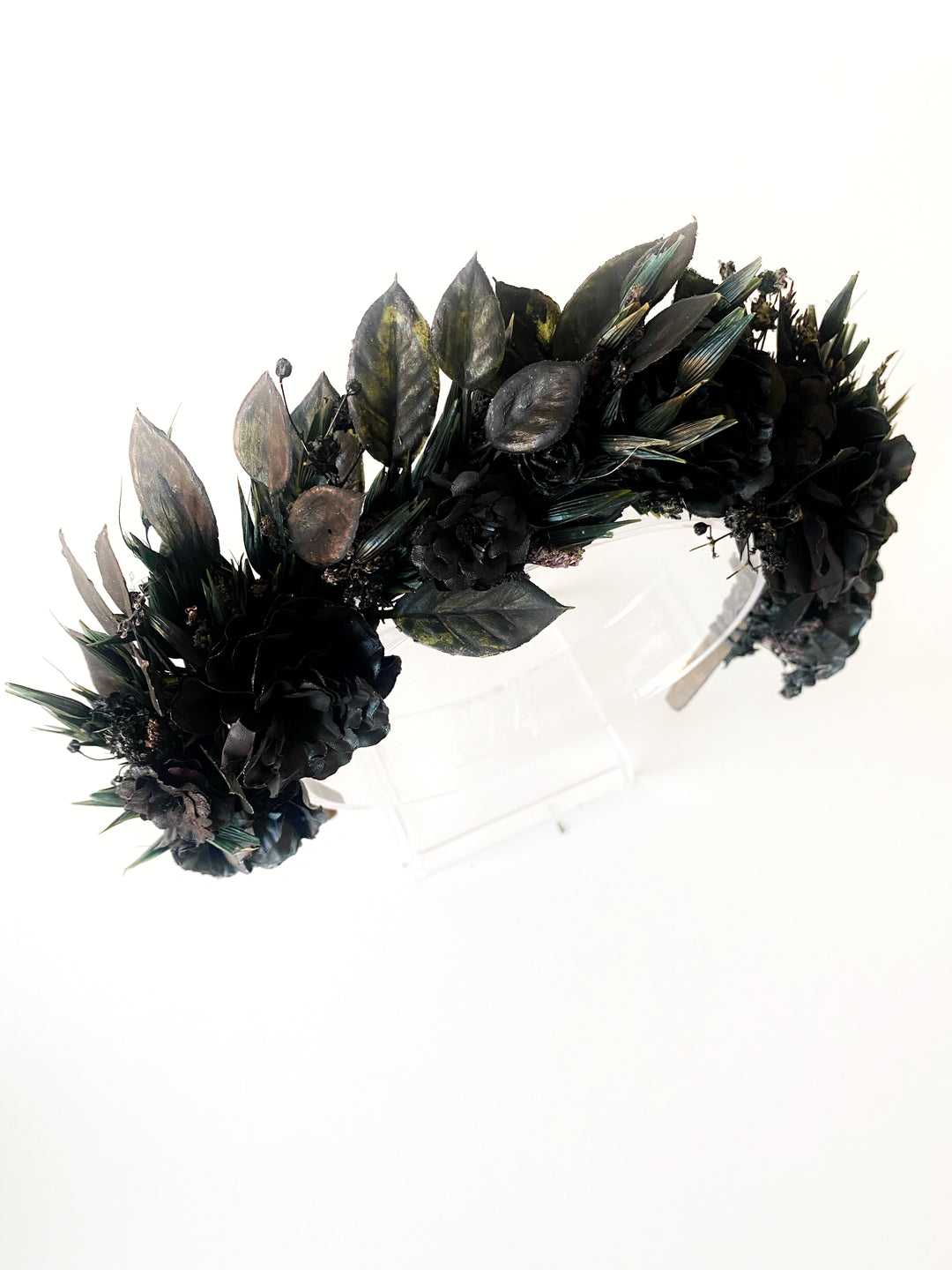 A black floral and leaf crown displayed on a clear acrylic stand against a plain white background.