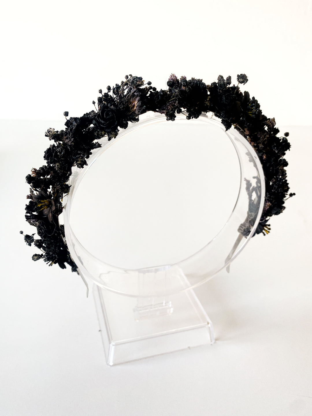 A black floral crown or headpiece displayed on a clear acrylic stand against a plain white background.