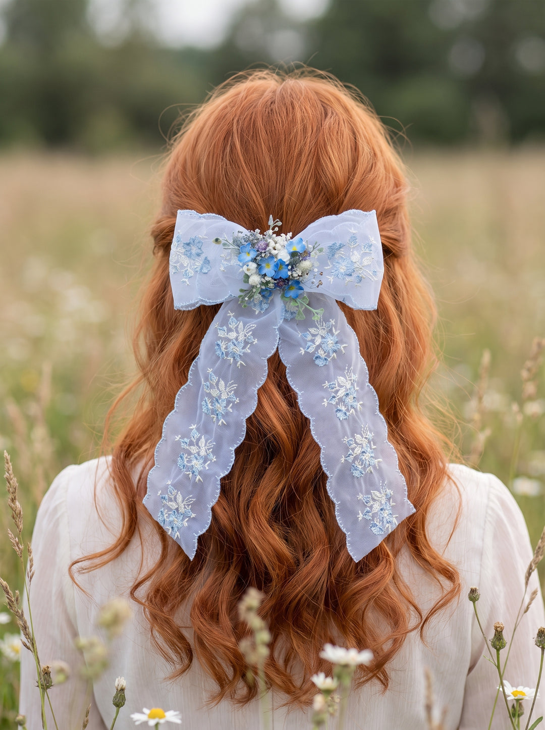 A person seen from behind wearing a large light blue lace hair bow with floral embellishments in a grassy outdoor field.