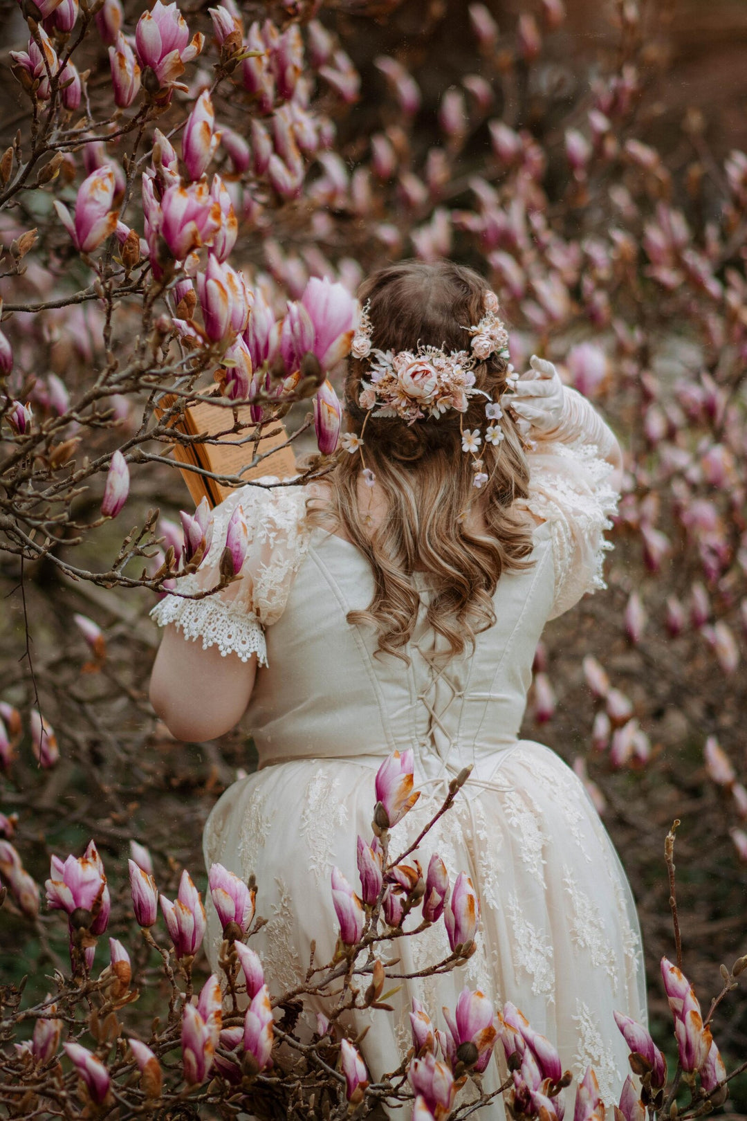 Woman in a white dress with floral headpiece standing among pink magnolia flowers