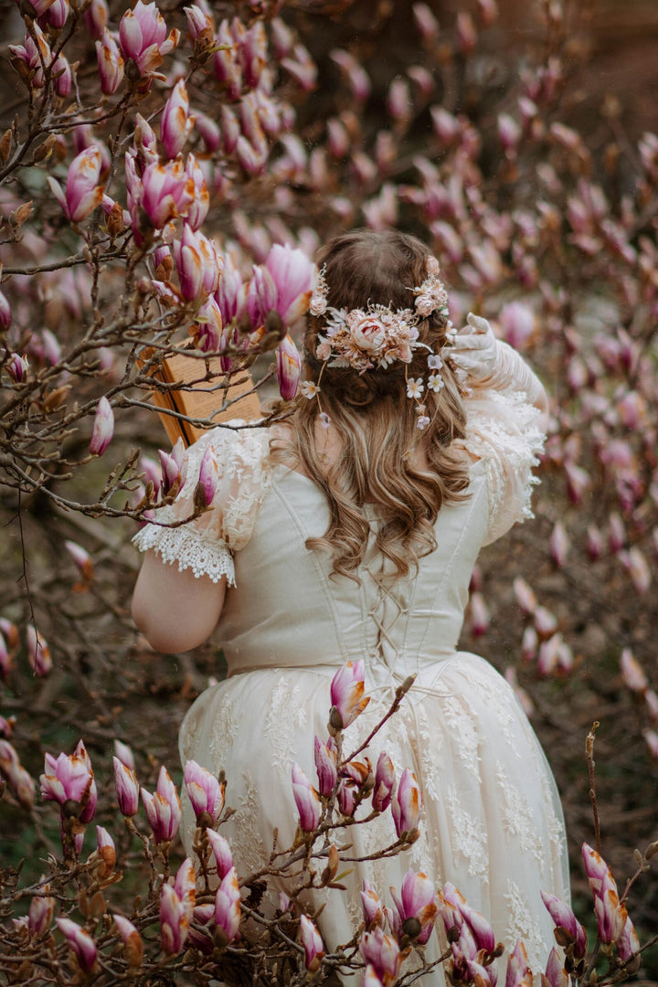 Woman in a white dress with floral headpiece standing among pink magnolia flowers
