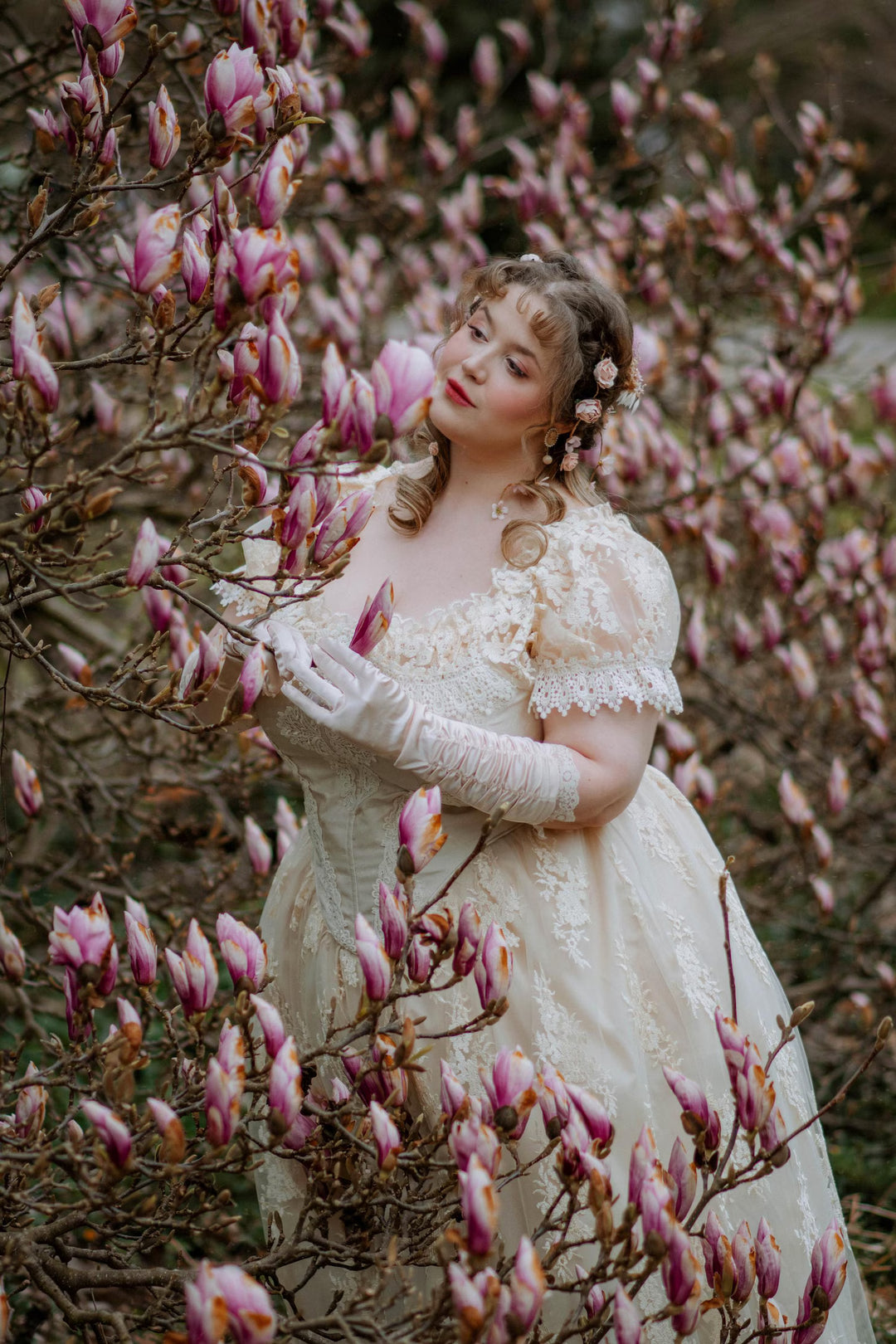 Woman in a vintage dress standing among pink flowering trees