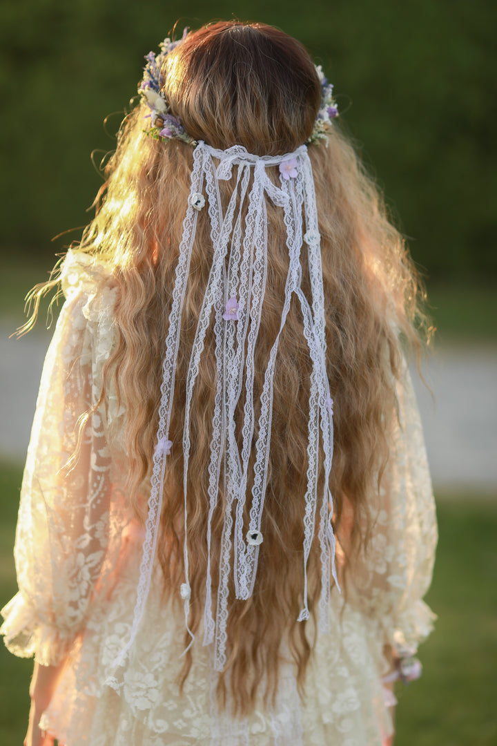 Person with long hair and decorative hair crown with long lace and flower veil in a natural setting