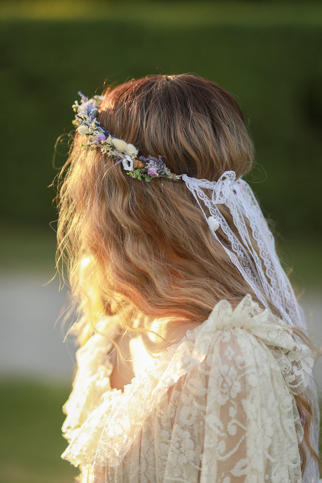 Person wearing a floral headpiece and lace veil with a blurred natural background