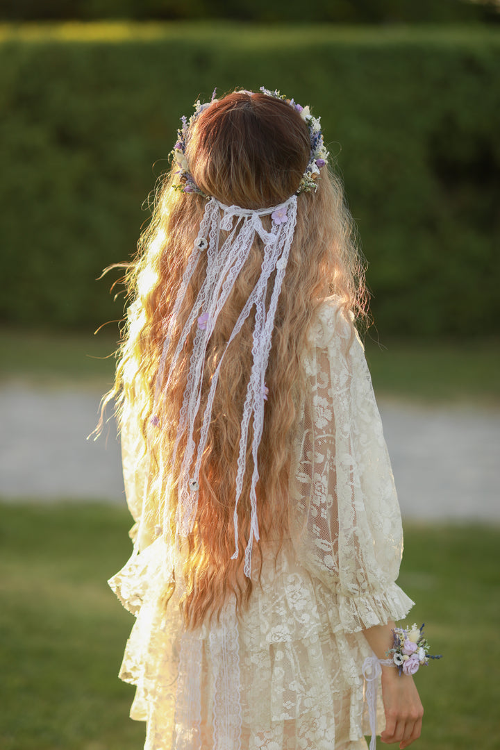Woman in a white dress with long hair and a floral crown standing outdoors.