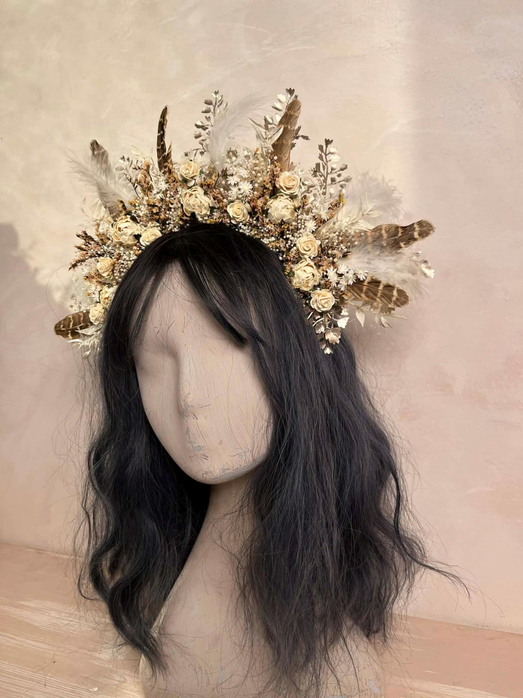 Mannequin head with black hair wearing a decorative floral and feather headpiece against a beige background