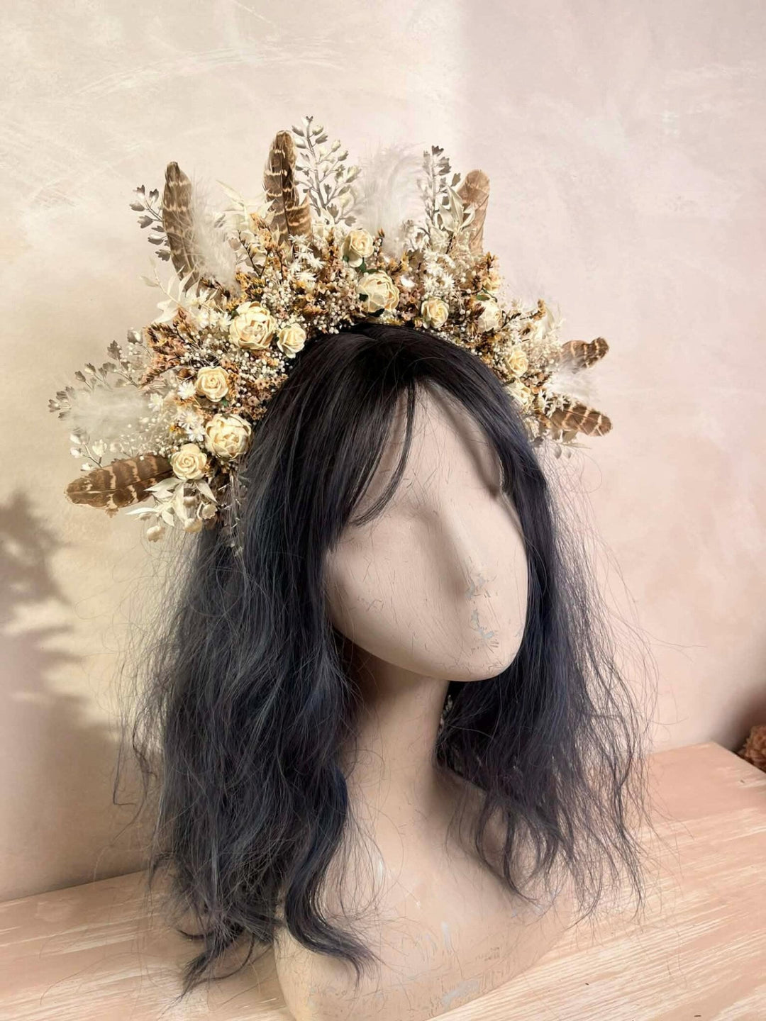 Mannequin head with dark hair wearing a decorative cream boho floral crown against a light background