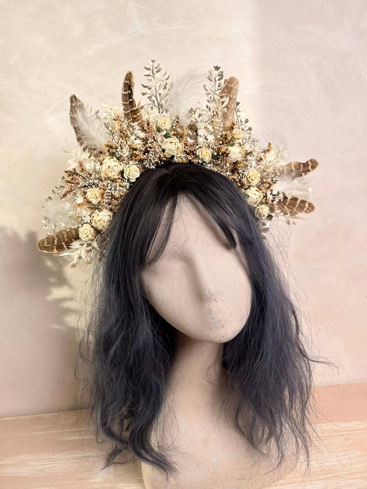Mannequin head with dark hair wearing a decorative headpiece with flowers and feathers on a neutral background.