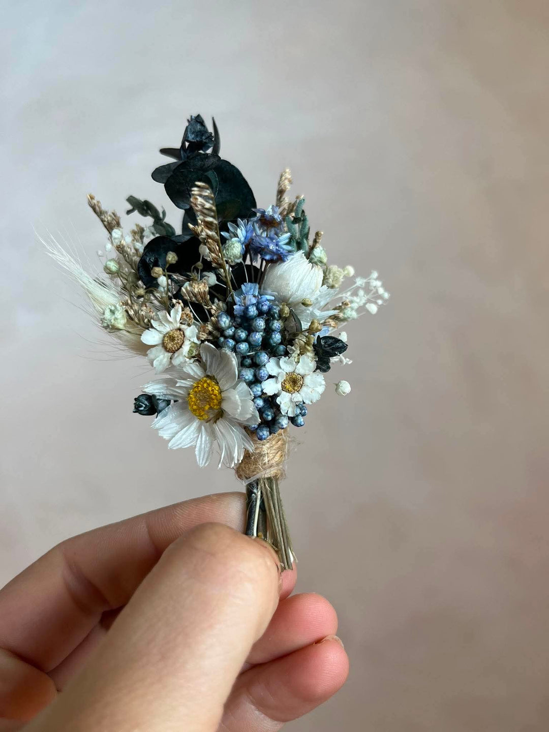 Handcrafted boutonniere made entirely from preserved and dried botanicals in a soft, warm palette - a central ivory daisy, delicate ixodia clusters, silvery eucalyptus sprigs, and wispy dried grasses.