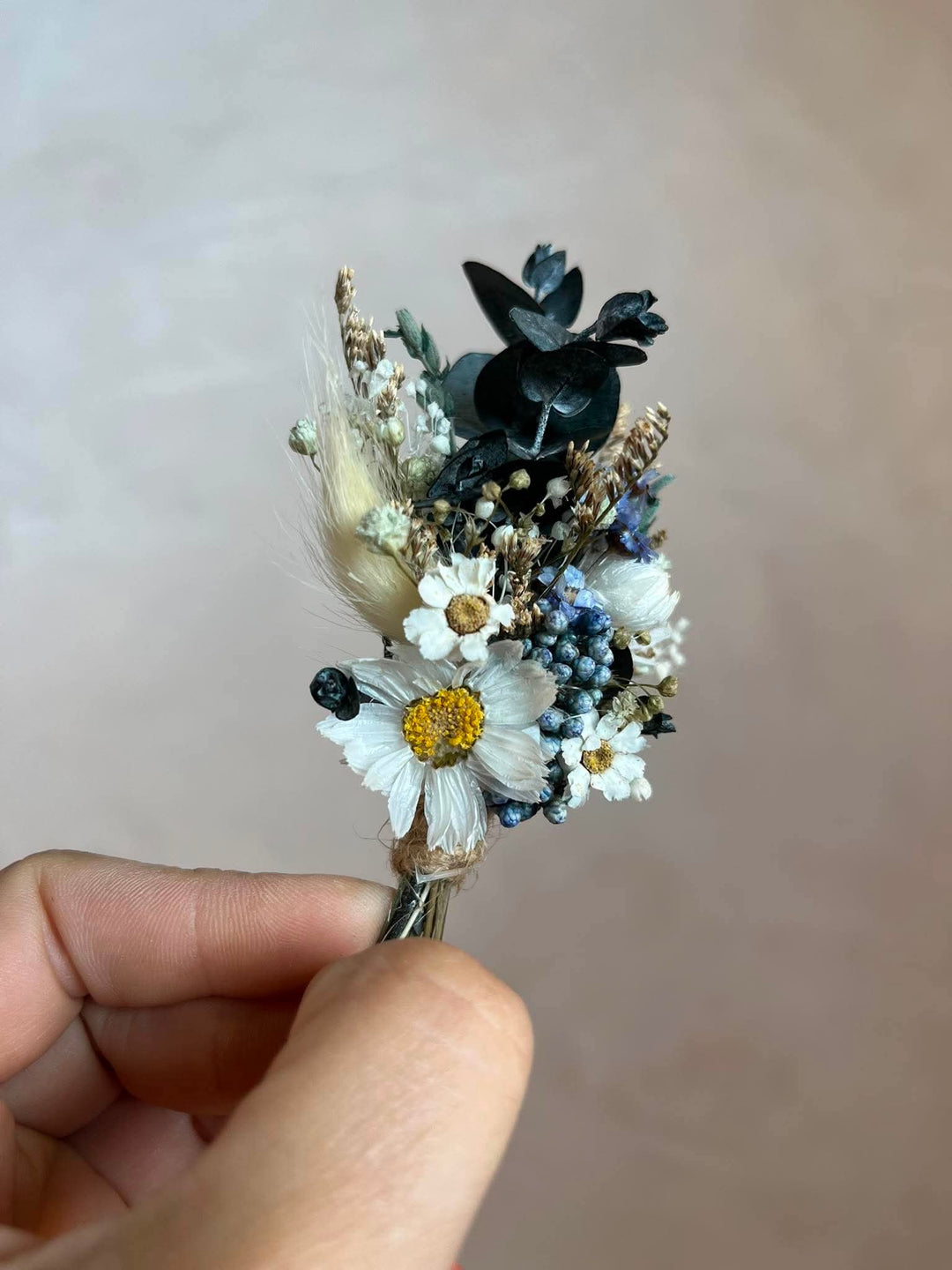 Handcrafted boutonniere made entirely from preserved and dried botanicals in a soft, warm palette - a central ivory daisy, delicate ixodia clusters, silvery eucalyptus sprigs, and wispy dried grasses.