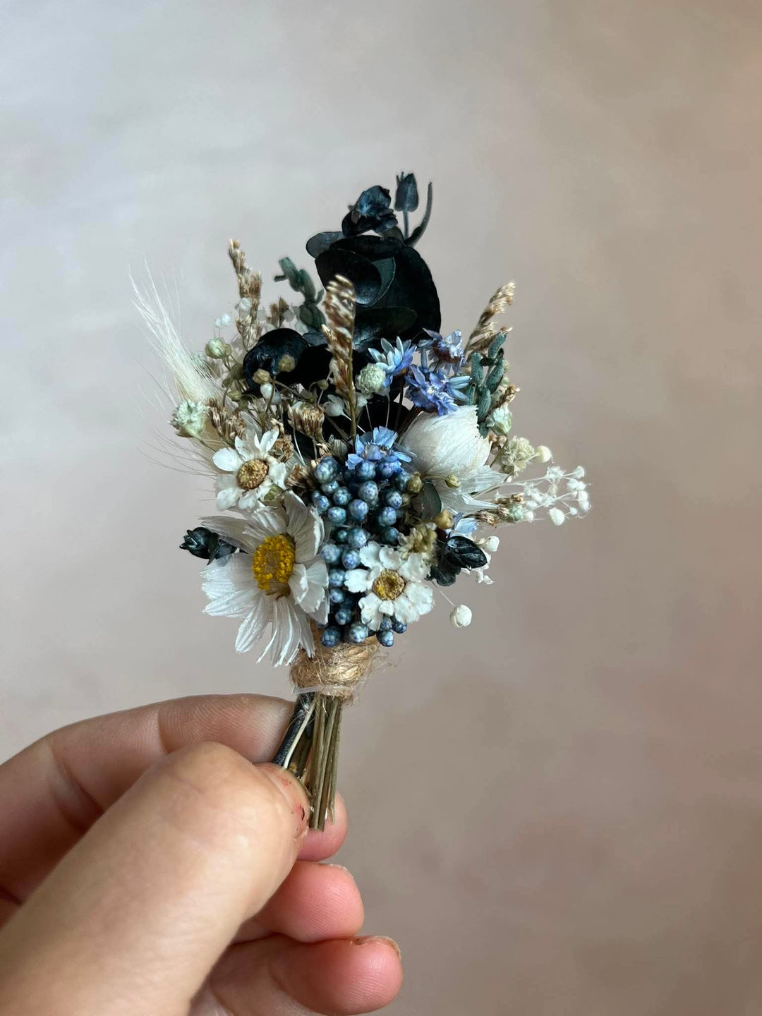 Handcrafted boutonniere made entirely from preserved and dried botanicals in a soft, warm palette - a central ivory daisy, delicate ixodia clusters, silvery eucalyptus sprigs, and wispy dried grasses.