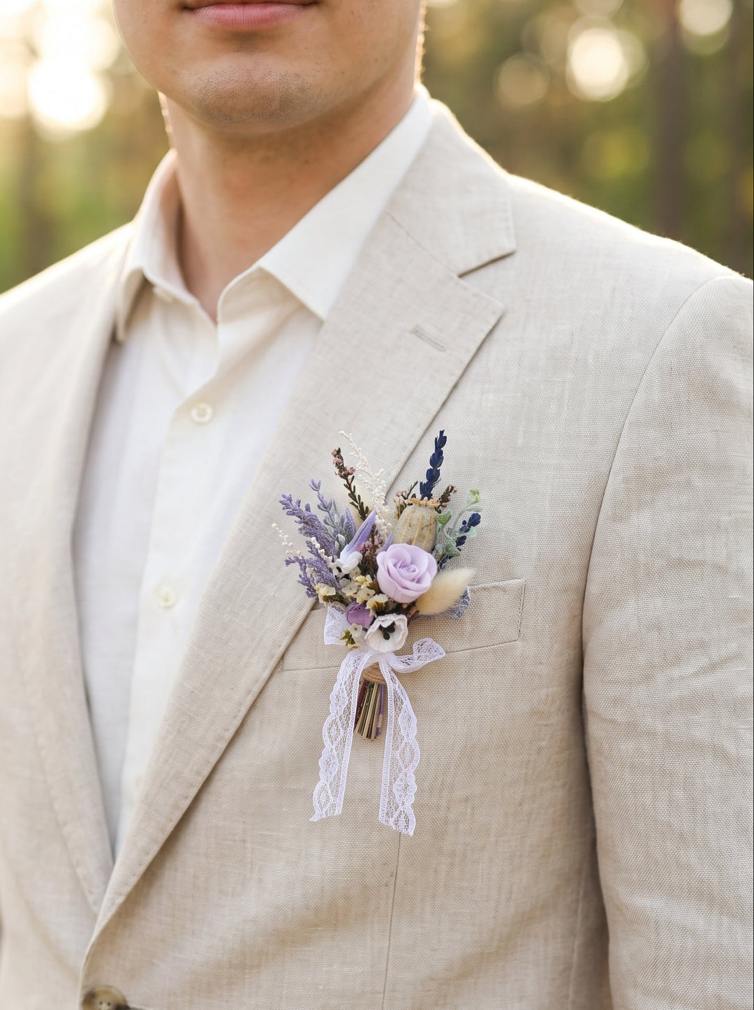 Man wearing a beige suit with a floral boutonniere on a blurred natural background