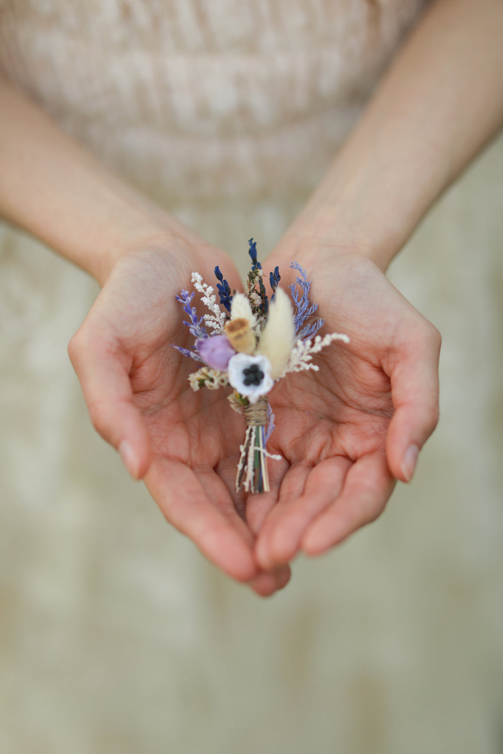 Hands holding a small floral arrangement against a blurred background
