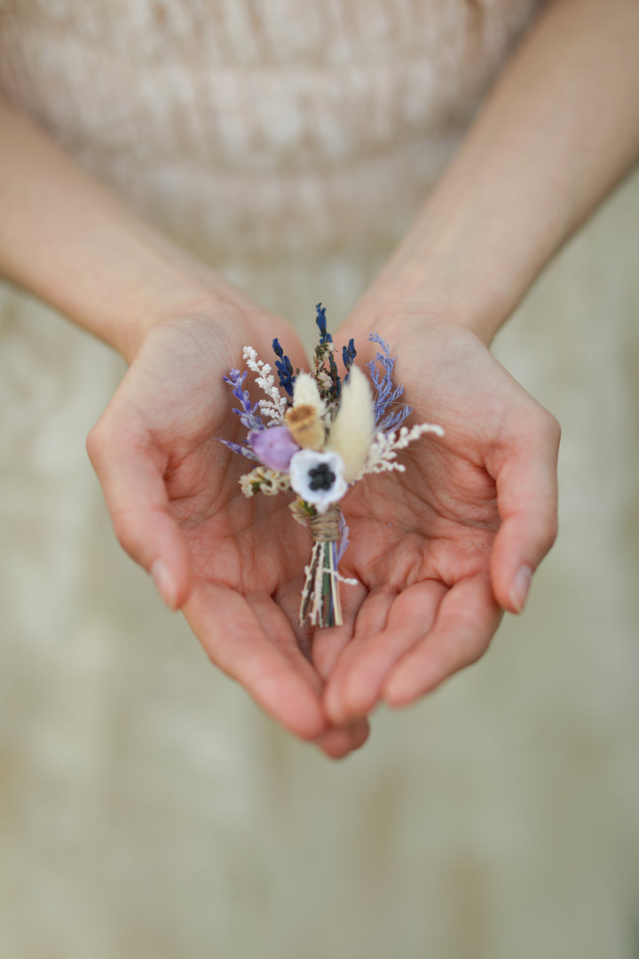 Hands holding a small floral arrangement against a blurred background