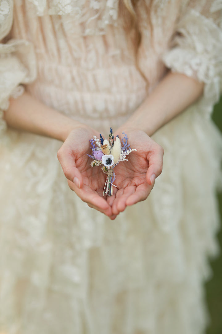 Person holding a small bouquet of flowers in their hands, wearing a light-colored dress.