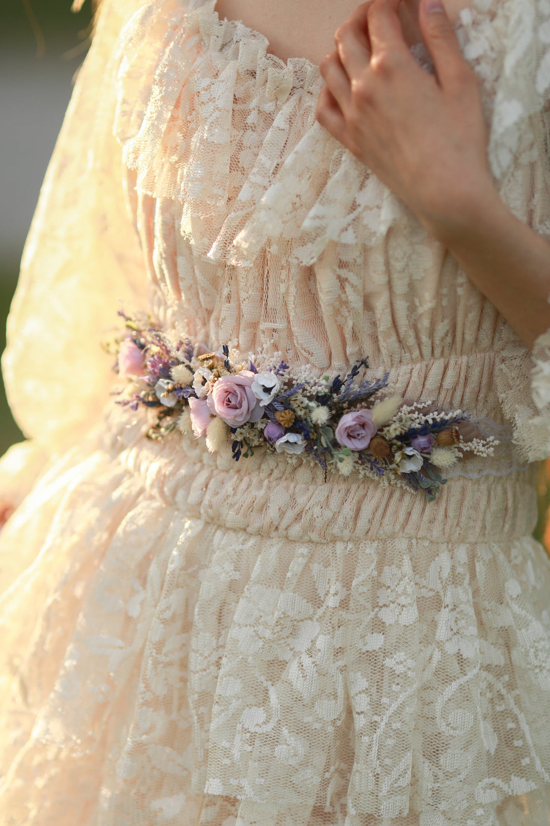 Close-up of a lace dress with a floral belt with anemone and roses in purple and cream tones. 
