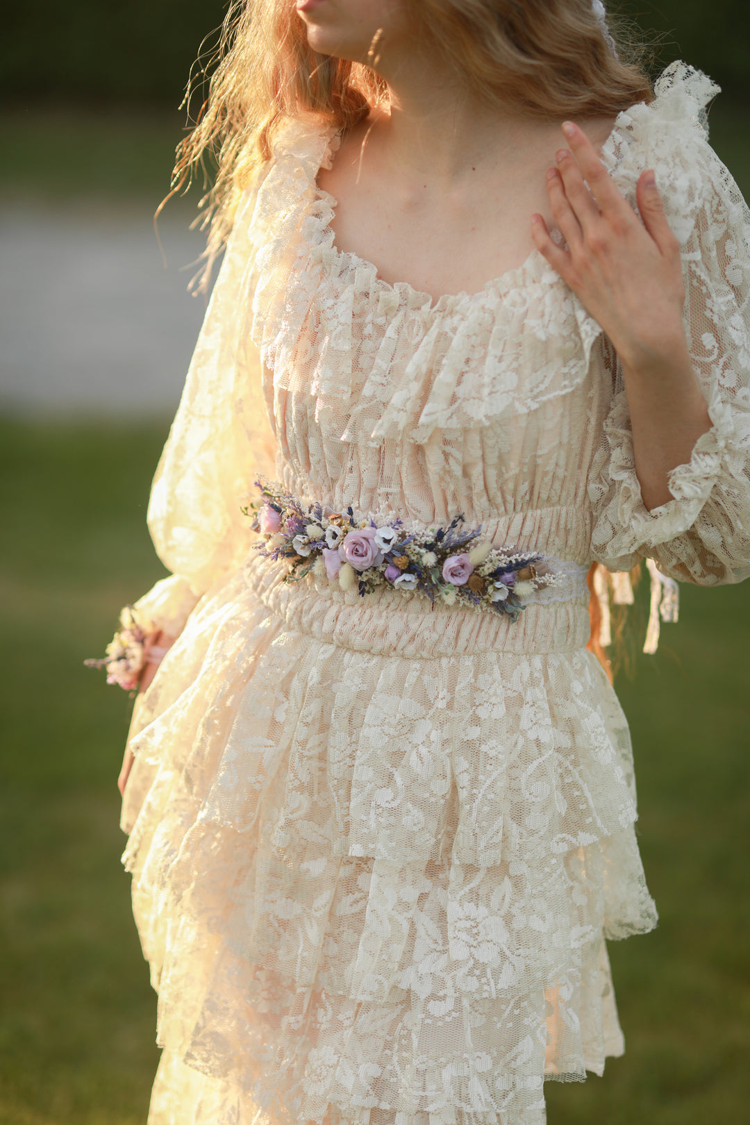 Woman wearing a lace dress with a floral belt in a natural setting