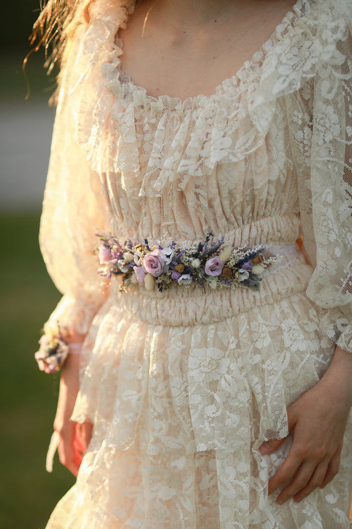Close-up of a person wearing a lace dress with a floral belt against a blurred natural background