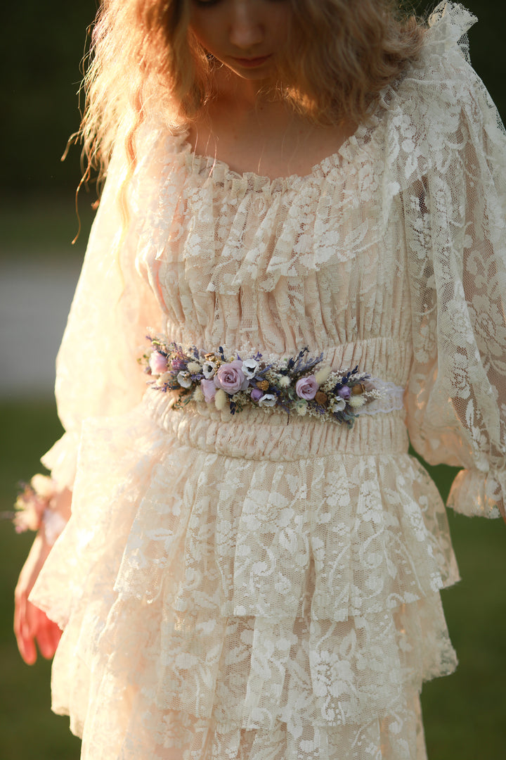 Woman wearing a lace dress with a floral belt in a natural setting