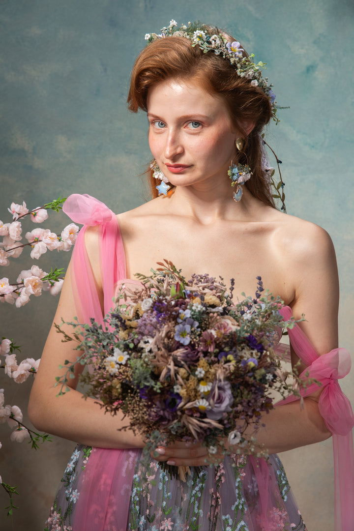 Woman holding a bouquet of flowers with a floral headpiece against a textured blue background