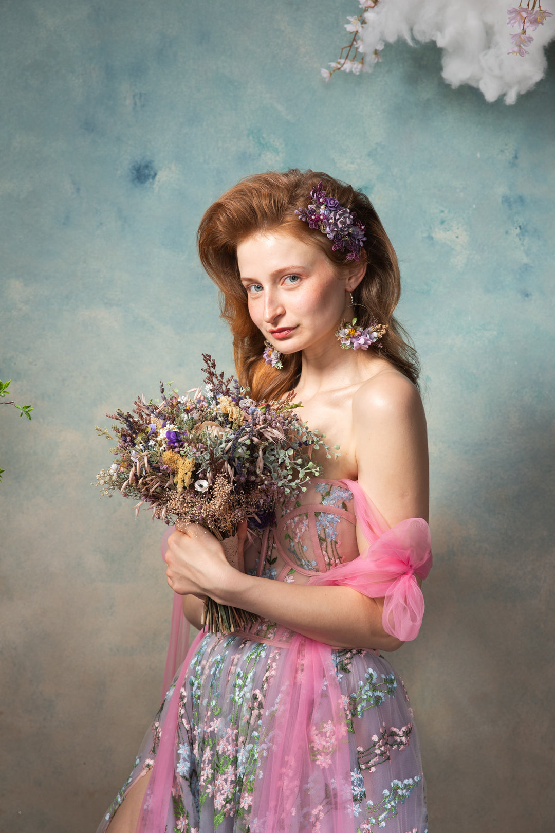Woman in a floral dress holding a bouquet of flowers against a textured blue background