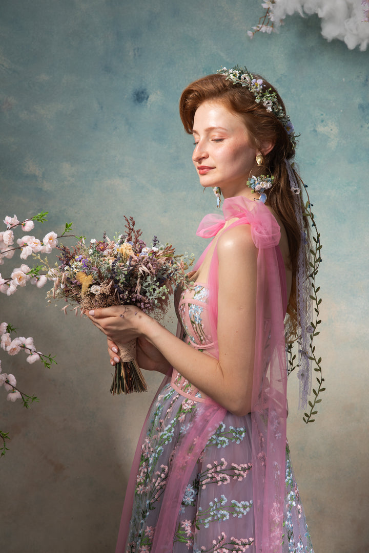 Woman in a floral dress holding flowers against a textured blue and gray background