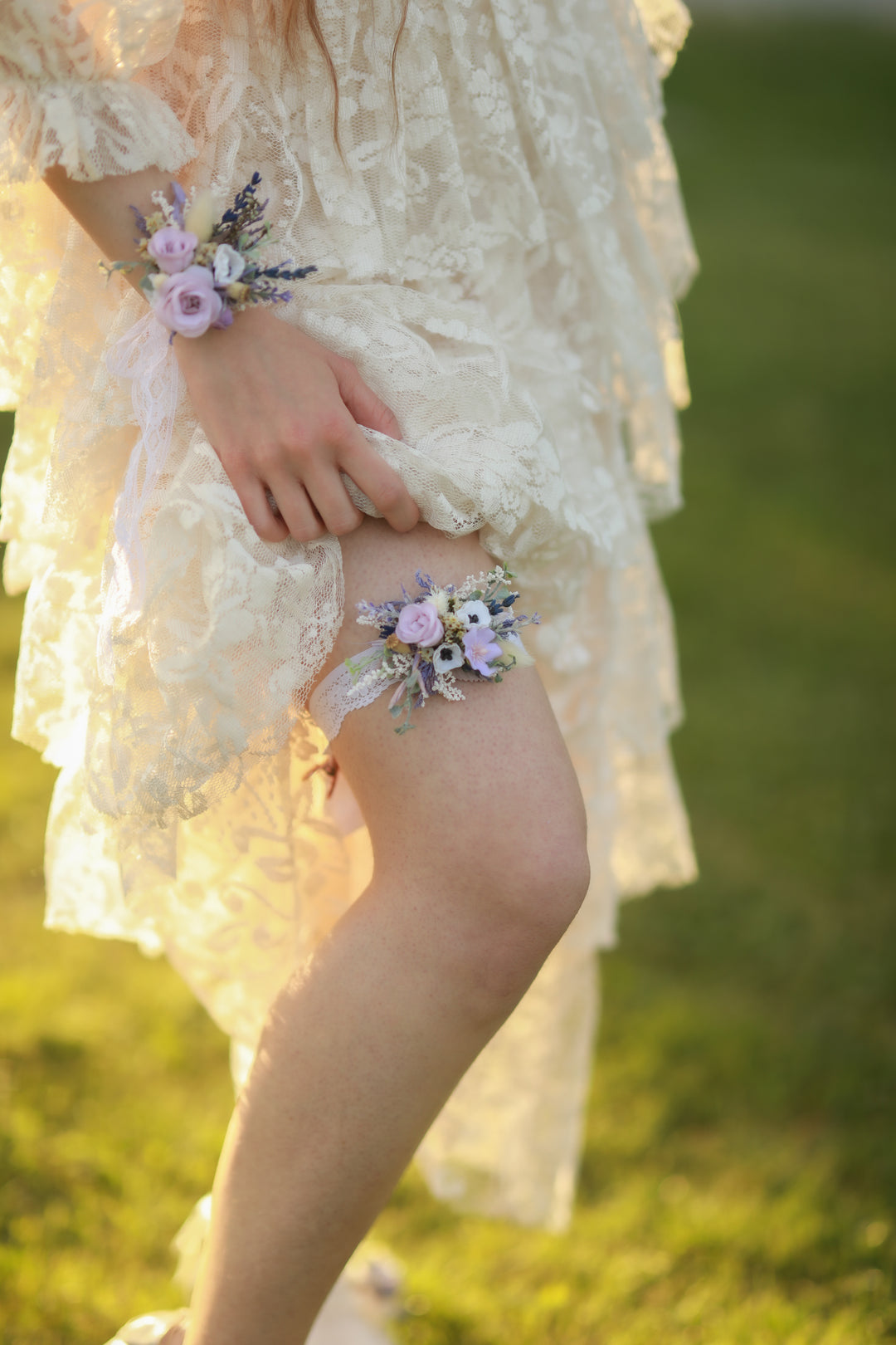 Person wearing a lace dress with floral wrist corsage and garter in a grassy field.