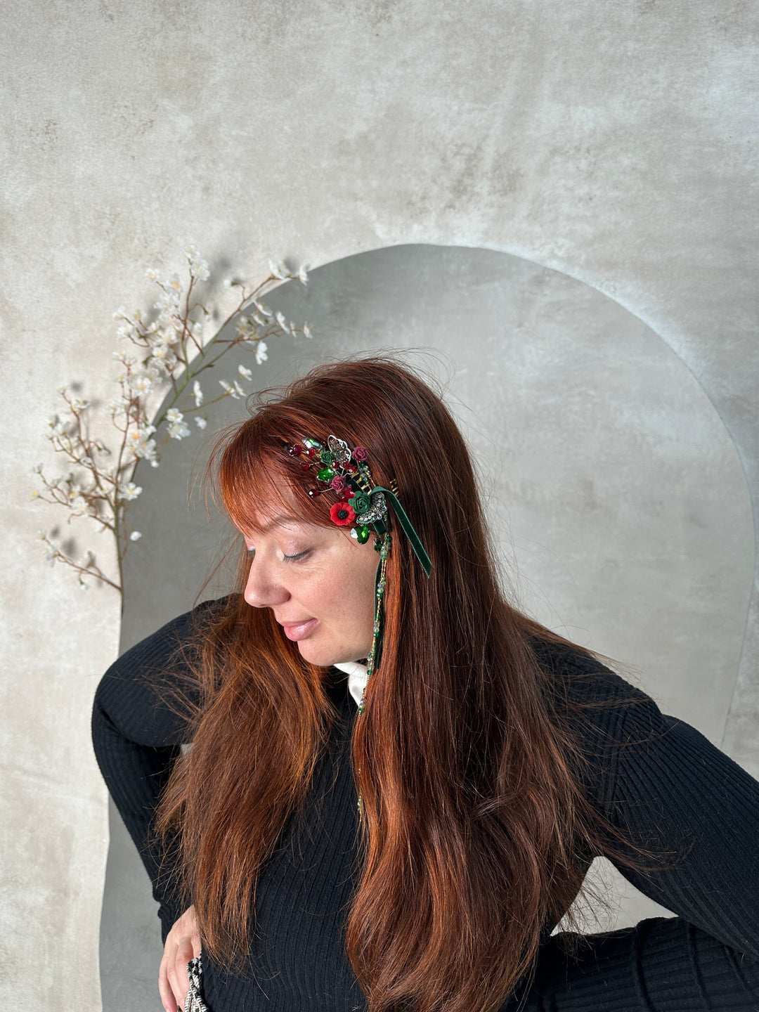 A woman with long brown hair wearing a decorative green headpiece with red poppy, photographed from above on a textured light gray surface.